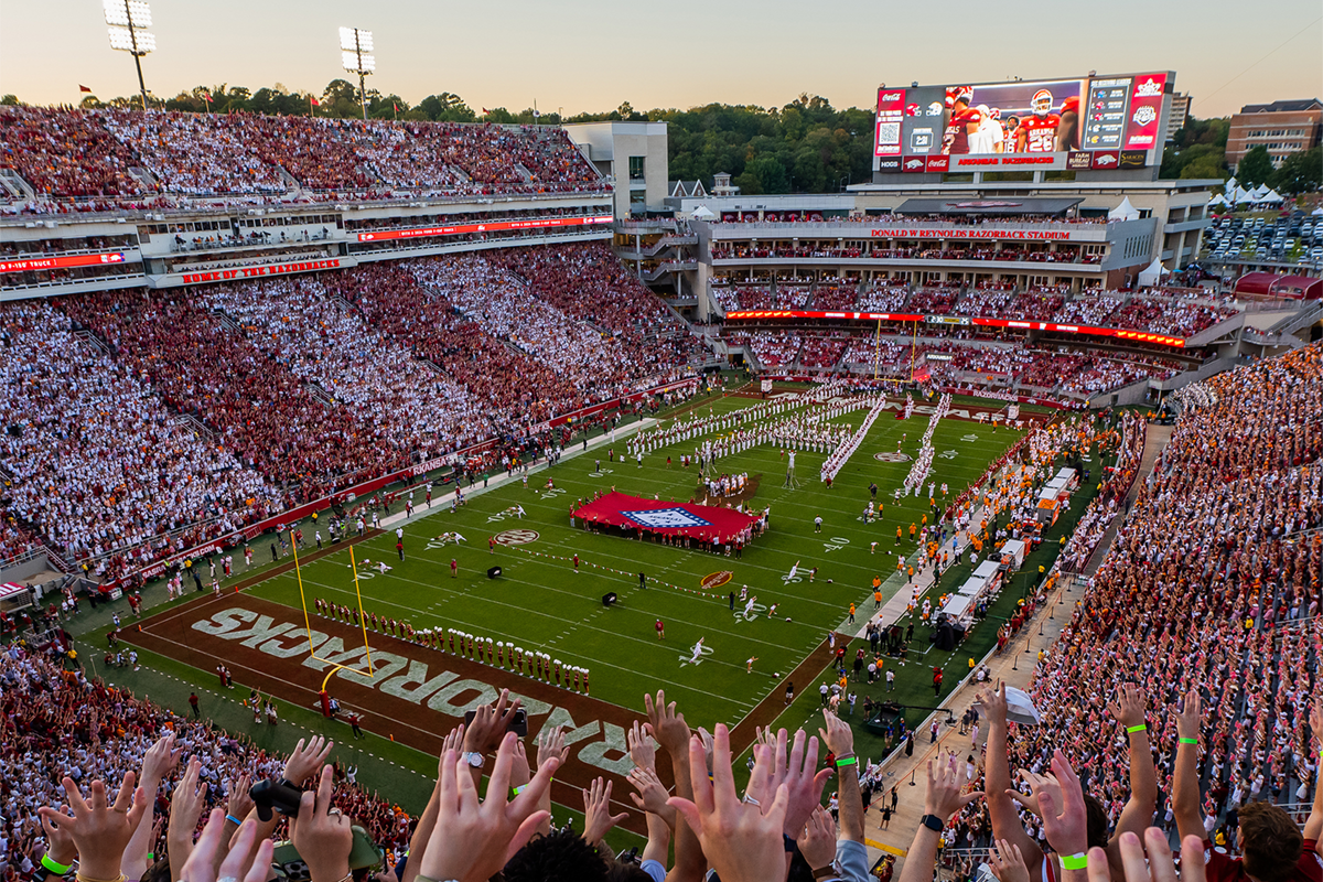 Razorback fans in the packed stadium with arms in the air watching football game