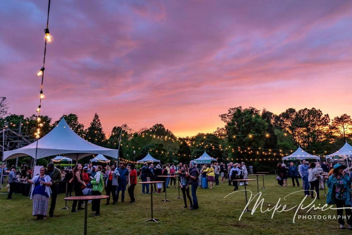 People eating around tables at a party under tents as the sun sets in a garden