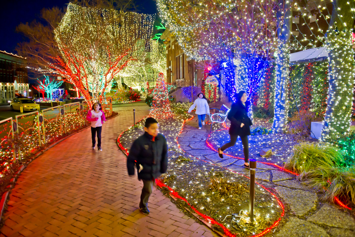children running on brick path with christmas lights hung in trees all around them
