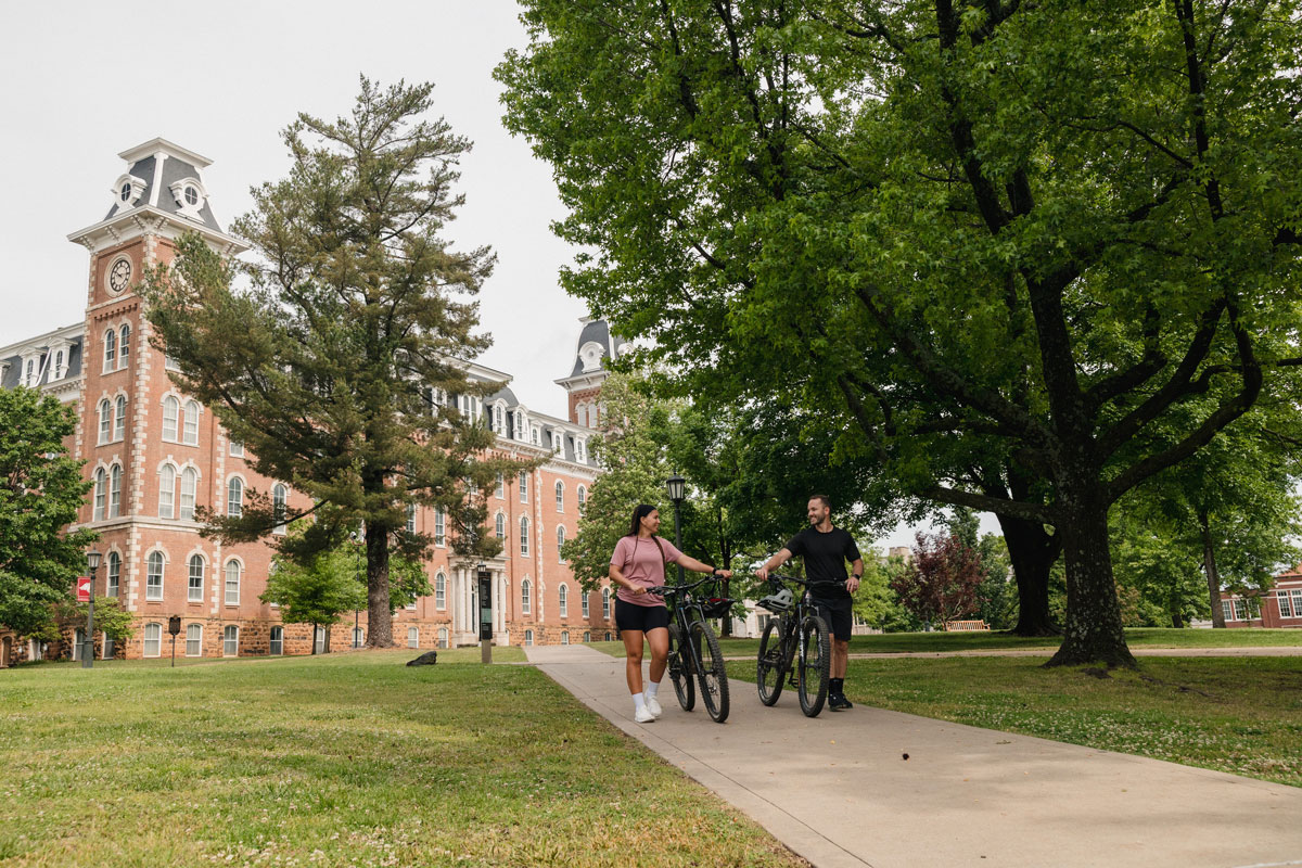 students walking alongside bikes on University of Arkansas campus in front of Old Main