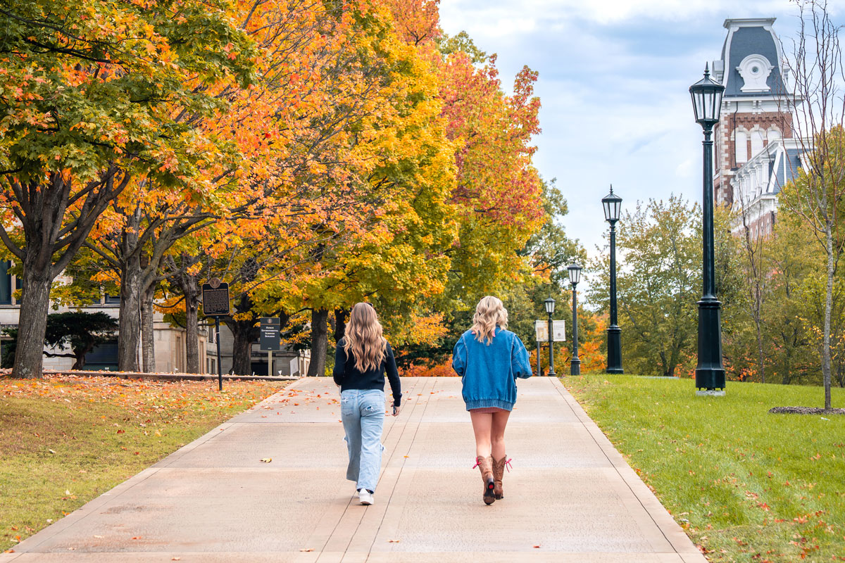 two women walking on the University of Arkansas campus in the fall with Old Main in the background